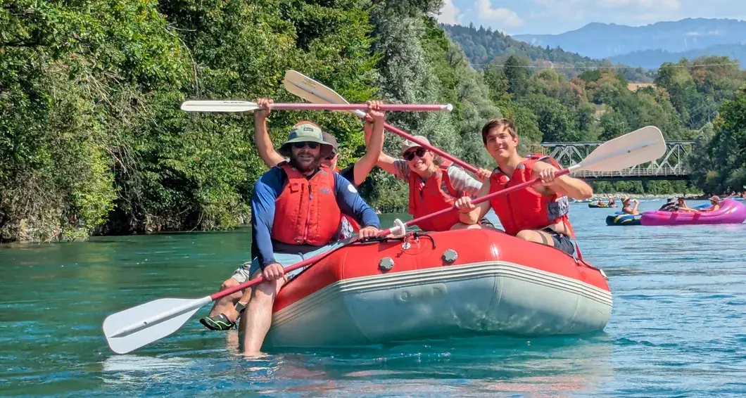 Drei Personen mit Schwimmwesten paddeln jubelnd in einem roten Schlauchboot auf der Aare