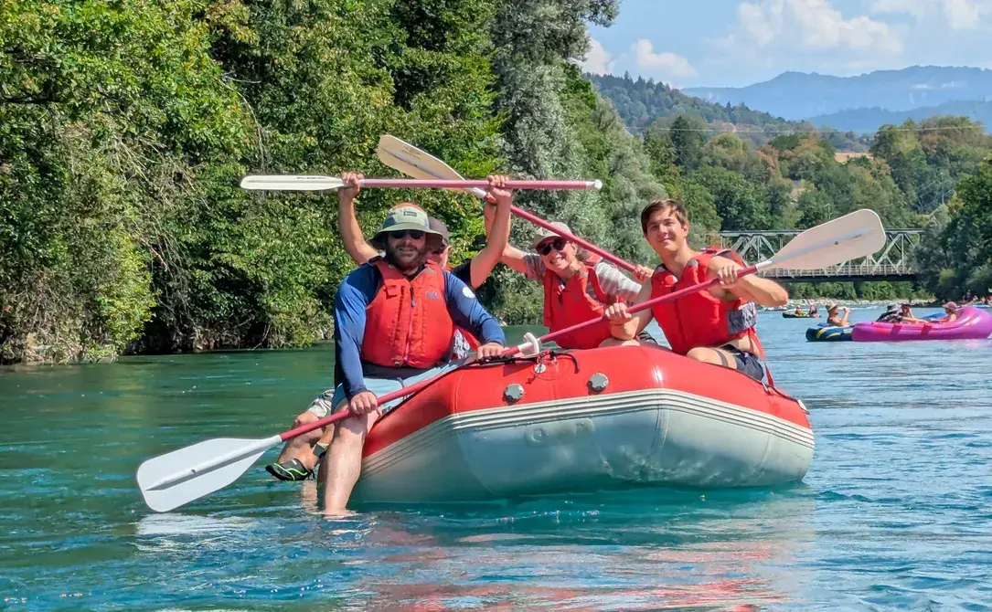 Drei Personen mit Schwimmwesten paddeln jubelnd in einem roten Schlauchboot auf der Aare