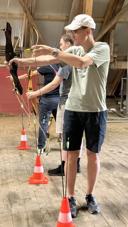 Thomas Werthmüller zielt beim Bogenschiessen in der Scheune, Pfeile stecken in Pylonen am Boden