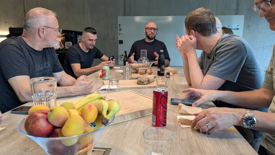 Previon-Team beim gemeinsamen Mittagessen mit Sandwiches und Früchten in der Bürolounge, ein Kollege spricht stehend