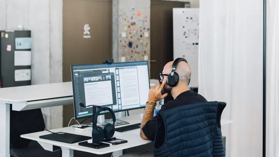Eine Person mit Kopfhörern, die an einem Computer mit zwei Bildschirmen in einem modern eingerichteten Büro arbeitet.