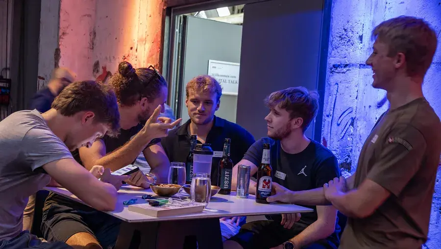 Junge Männer sitzen an einem Stehtisch mit Getränken und unterhalten sich beim Digital Talk in Aarau