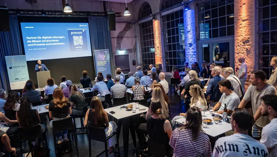 Publikum an Stehtischen verfolgt den Digital Talk in der Aeschbachhalle Aarau, auf der Leinwand die Previon-Slide.