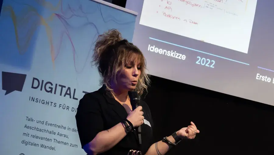 Referentin Cinzia Bonetta erklärt am Digital Talk mit Mikrofon in der Hand eine Ideenskizze auf der Leinwand hinter ihr.
