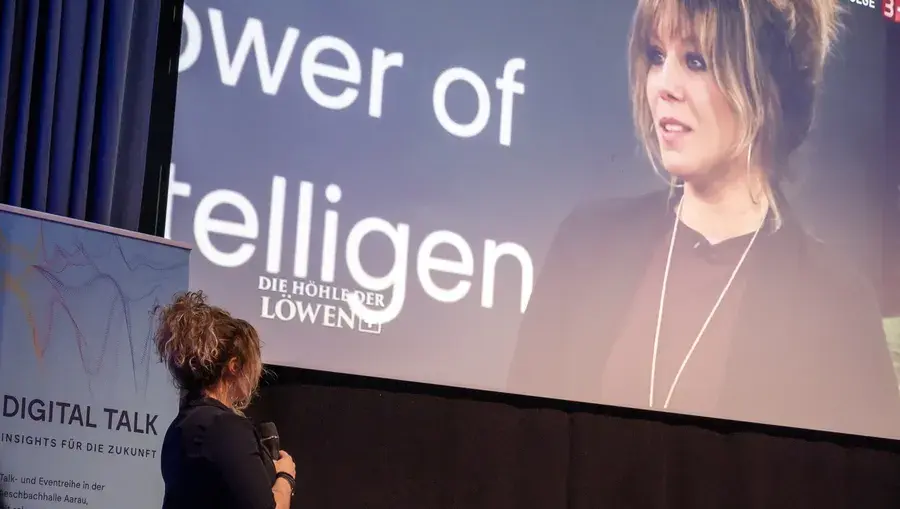 Referentin mit Mikrofon auf der Digital-Talk-Bühne vor einer Leinwand mit dem Titel «Power of Intelligence»., Höhle der Löwen.