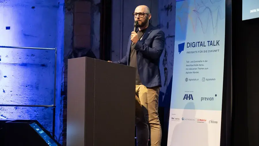 Claudio Scicchitano am Rednerpult neben dem Digital-Talk-Rollup in der Aeschbachhalle Aarau.